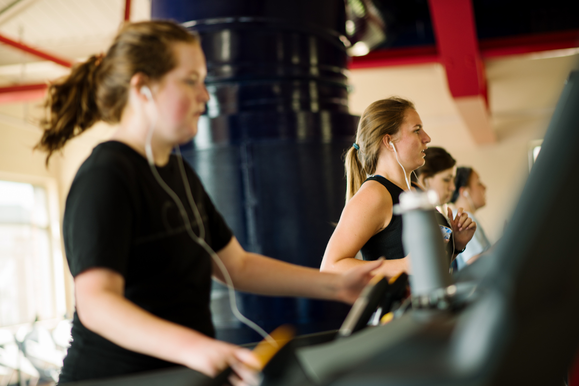 ${ Four patrons on a row of four treadmills on the track of the RecPlex Fitness center.  }